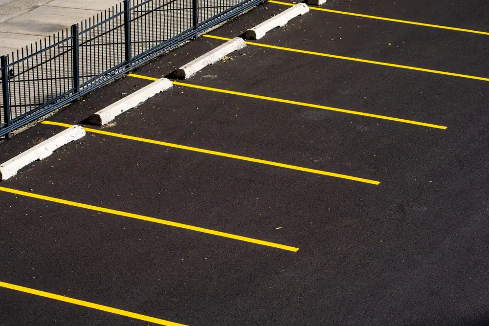 Dark sealcoated asphalt with fresh yellow parking stripes and wheel stops